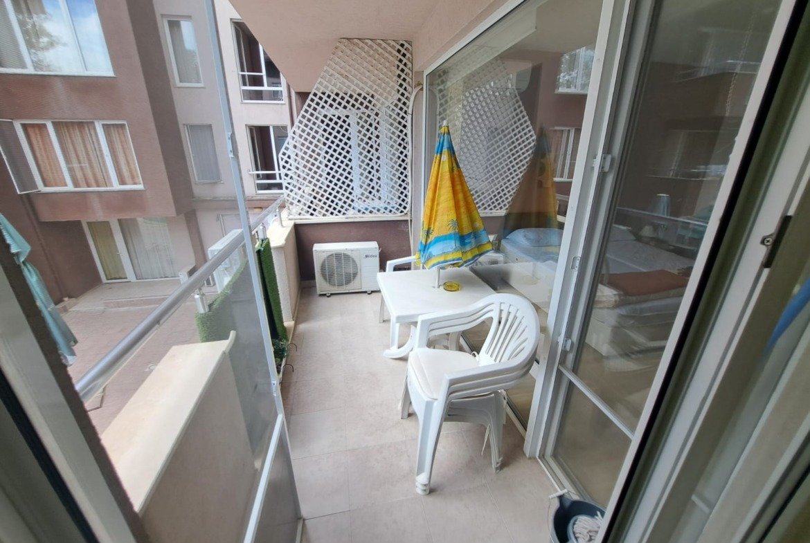 Балкон двухкомнатного апартамента с белыми пластиковыми креслами, столом и зонтом, в комплексе Stella Polaris, Болгария.