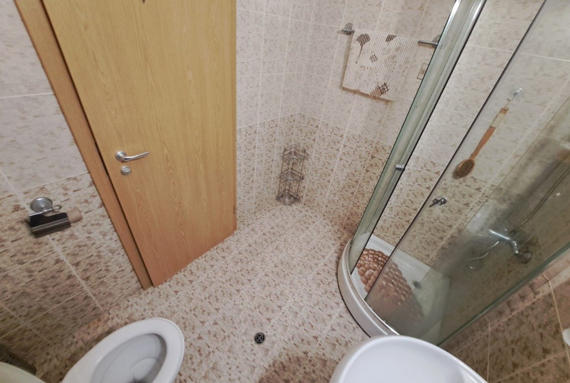 Современная ванная комната с душевой кабиной, унитазом и светлыми плитками в апартаменте в Болгарии.