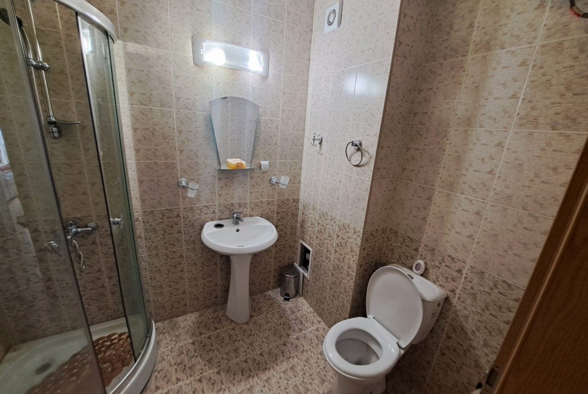 Современный санузел с душевой кабиной, умывальником и туалетом в двухкомнатном апартаменте в Болгарии.