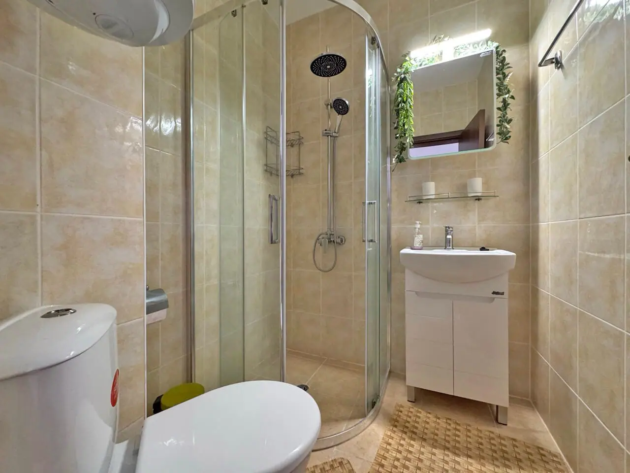 Современная ванная комната с душевой кабиной, умывальником и зелеными растениями, оформлена в светлых тонах.