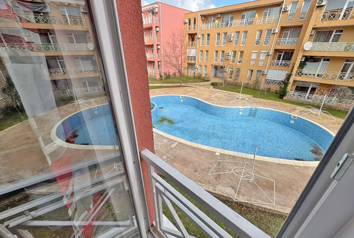 Вид из окна студии на бассейн комплекса Sunny Day 6 с голубой водой и окружением жилых корпусов.