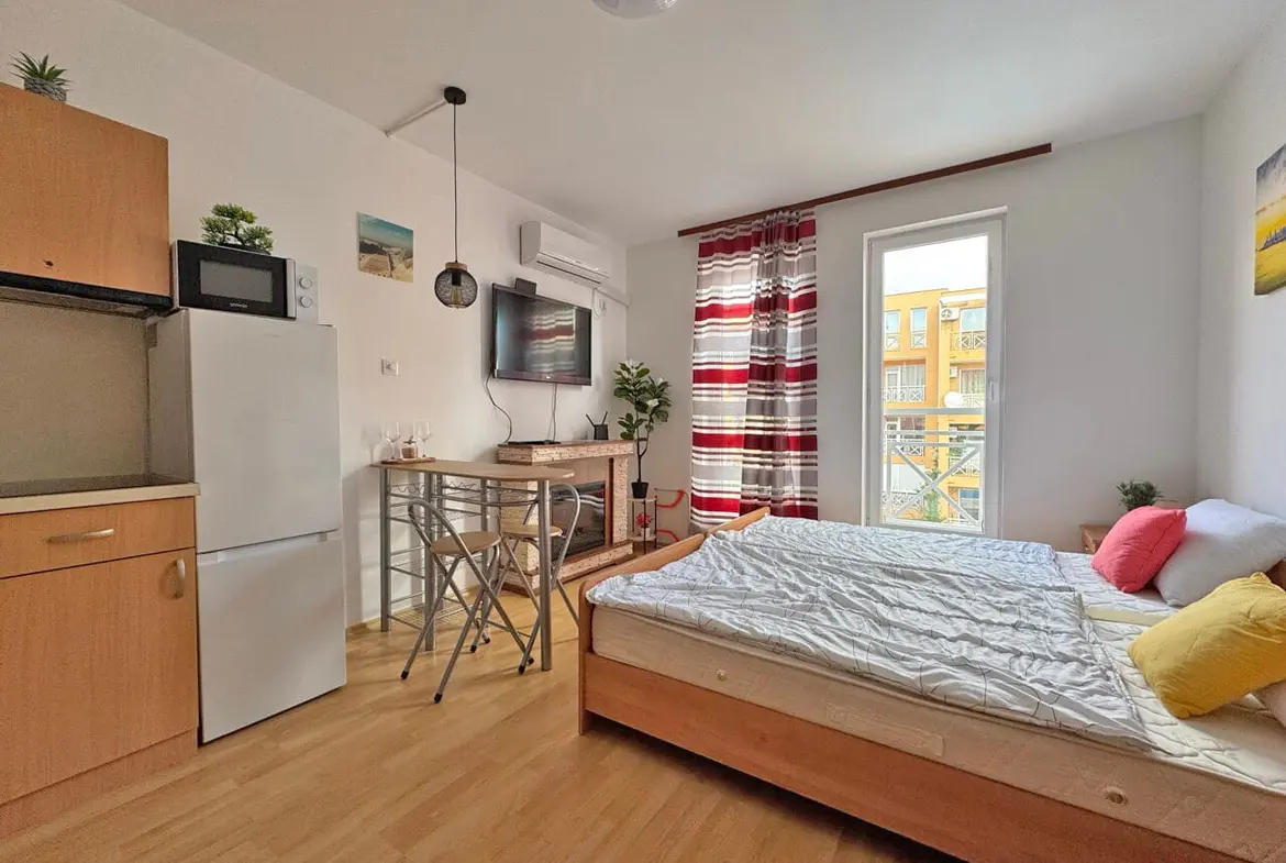 Уютная студия с кухонным уголком, двуспальной кроватью и яркими декоративными элементами, с окном на солнечный двор.