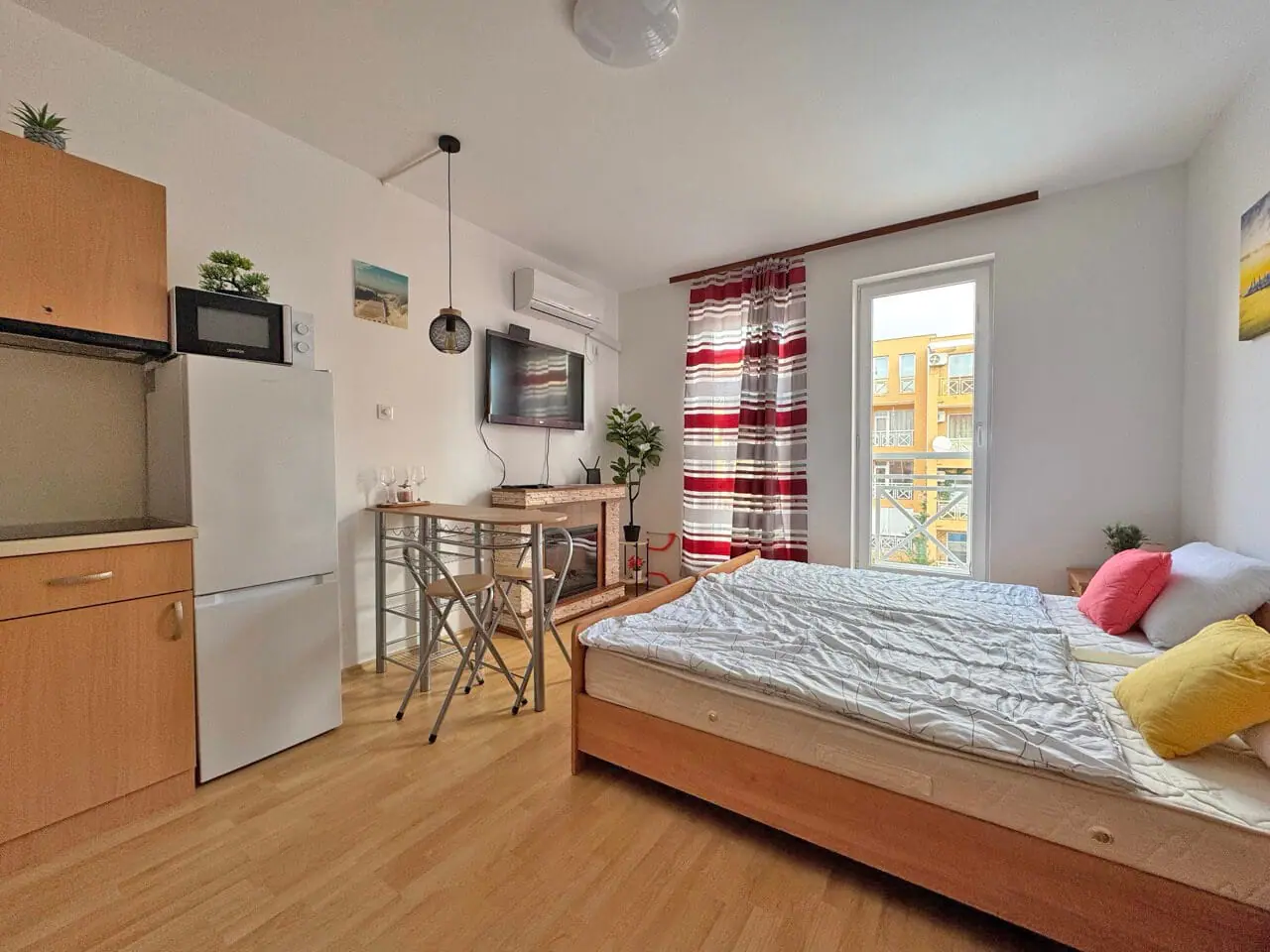 Уютная студия с кухонным уголком, двуспальной кроватью и яркими декоративными элементами, с окном на солнечный двор.