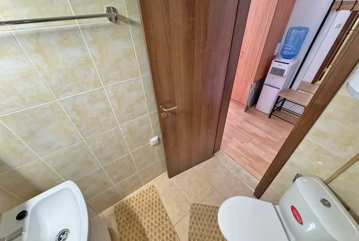 Современный Санузел с туалетом и умывальником, отделанный плиткой, в светлых тонах, с деревянными элементами и аксессуарами.