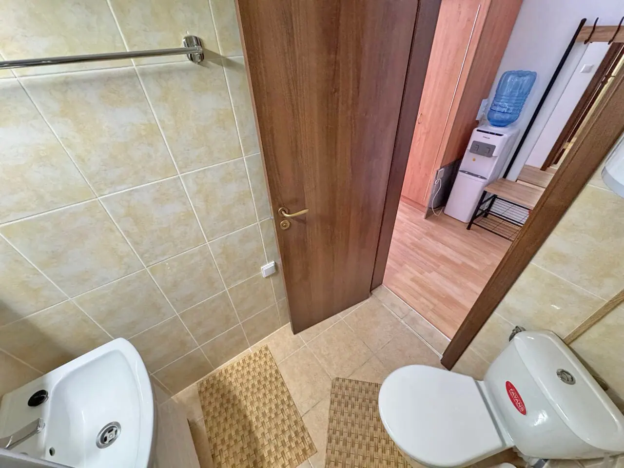 Современный Санузел с туалетом и умывальником, отделанный плиткой, в светлых тонах, с деревянными элементами и аксессуарами.