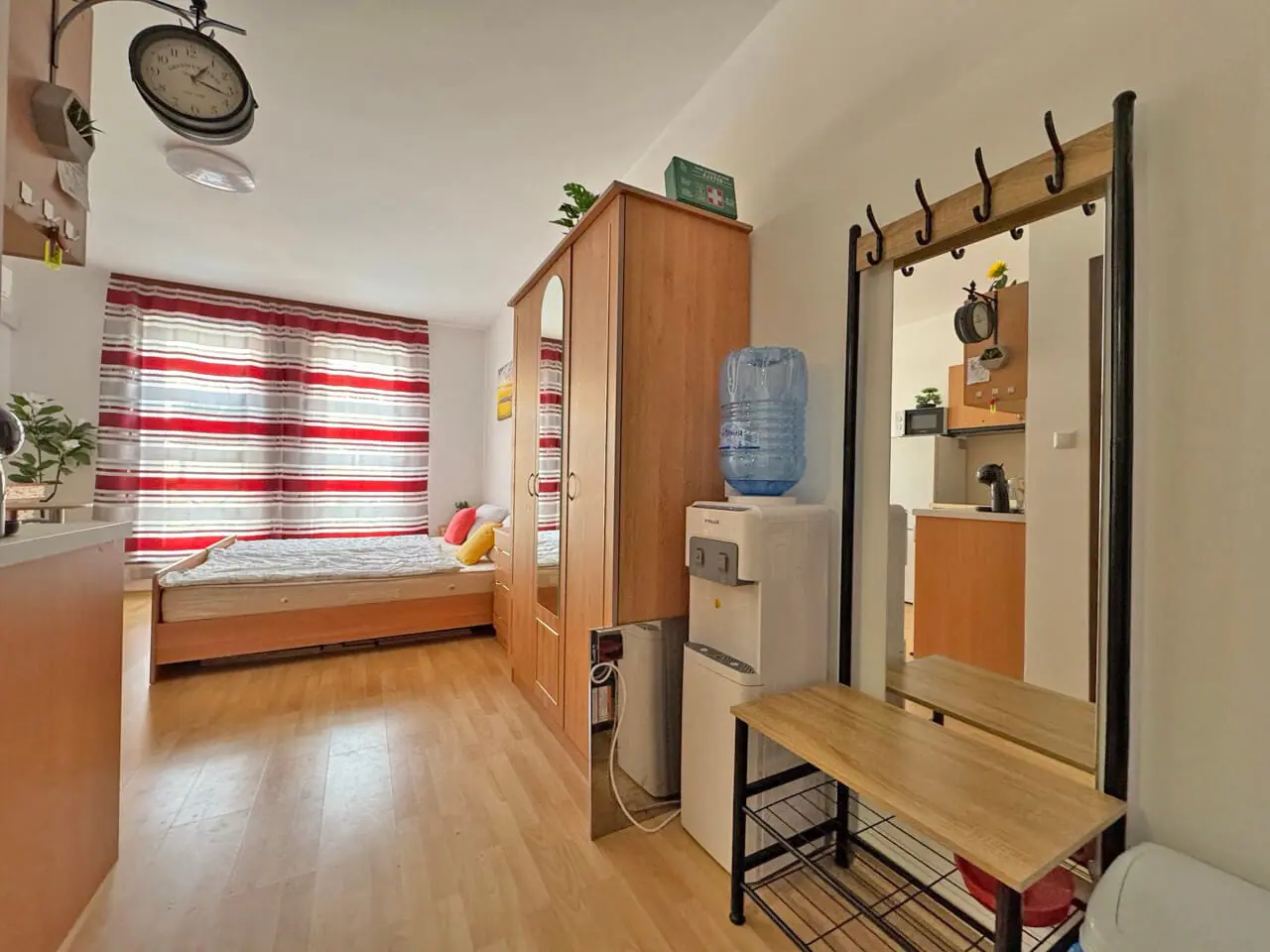 Уютная студия с двуспальной кроватью, деревянной мебелью и зеркалом, яркими шторами и мини-кухней.