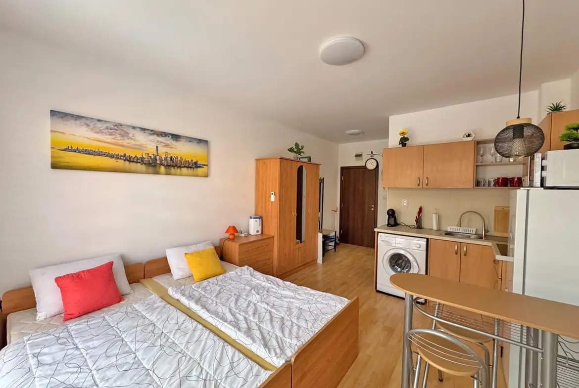 Современная студия с двумя кроватями, кухонной зоной и бытовой техникой, оформленная в светлых тонах.