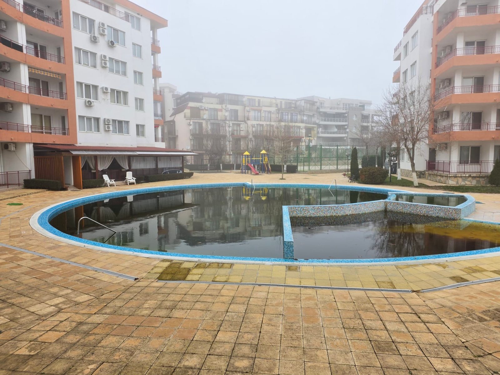 Двухкомнатный апартамент с видом на бассейн в Riviera Fort Beach Двухкомнатный апартамент с видом на бассейн, окруженный зданиями комплекса Riviera Fort Beach, в туманной обстановке.