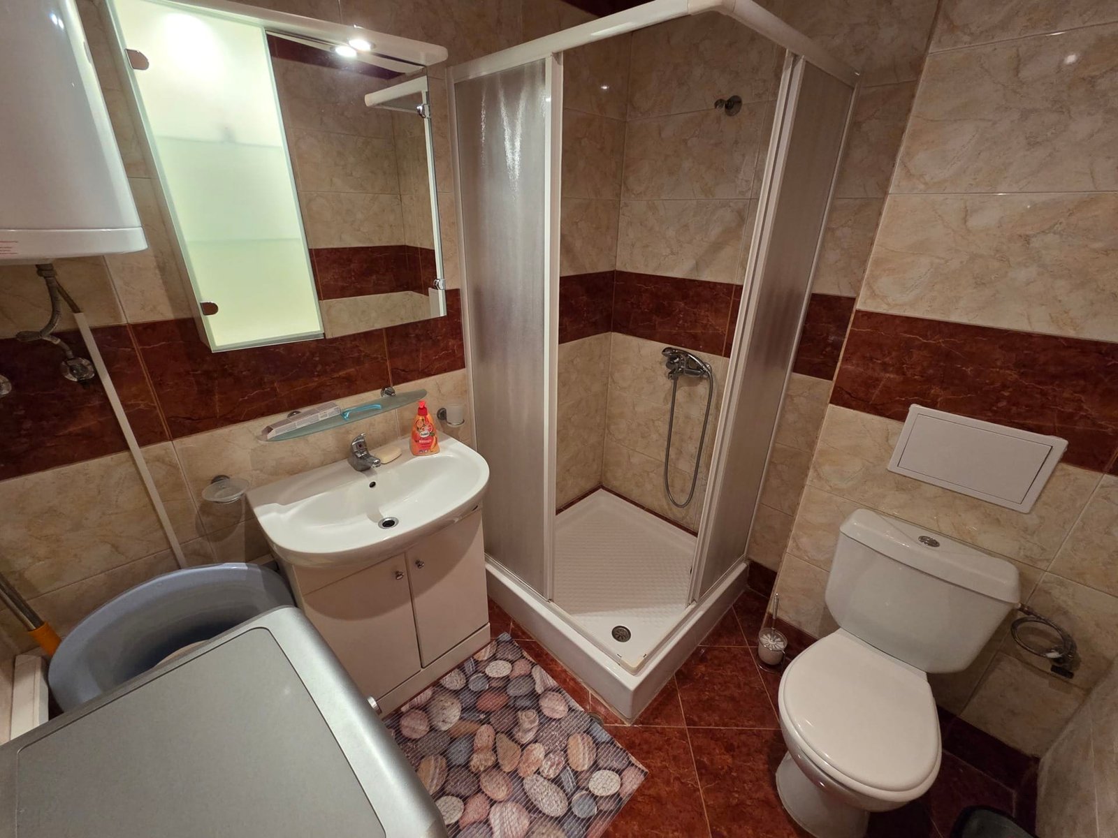 Душевая и санузел в двухкомнатном апартаменте Riviera Fort Beach Современная ванная комната с душевой кабиной, умывальником, унитазом и стиральной машиной, оформленная в теплых тонах.