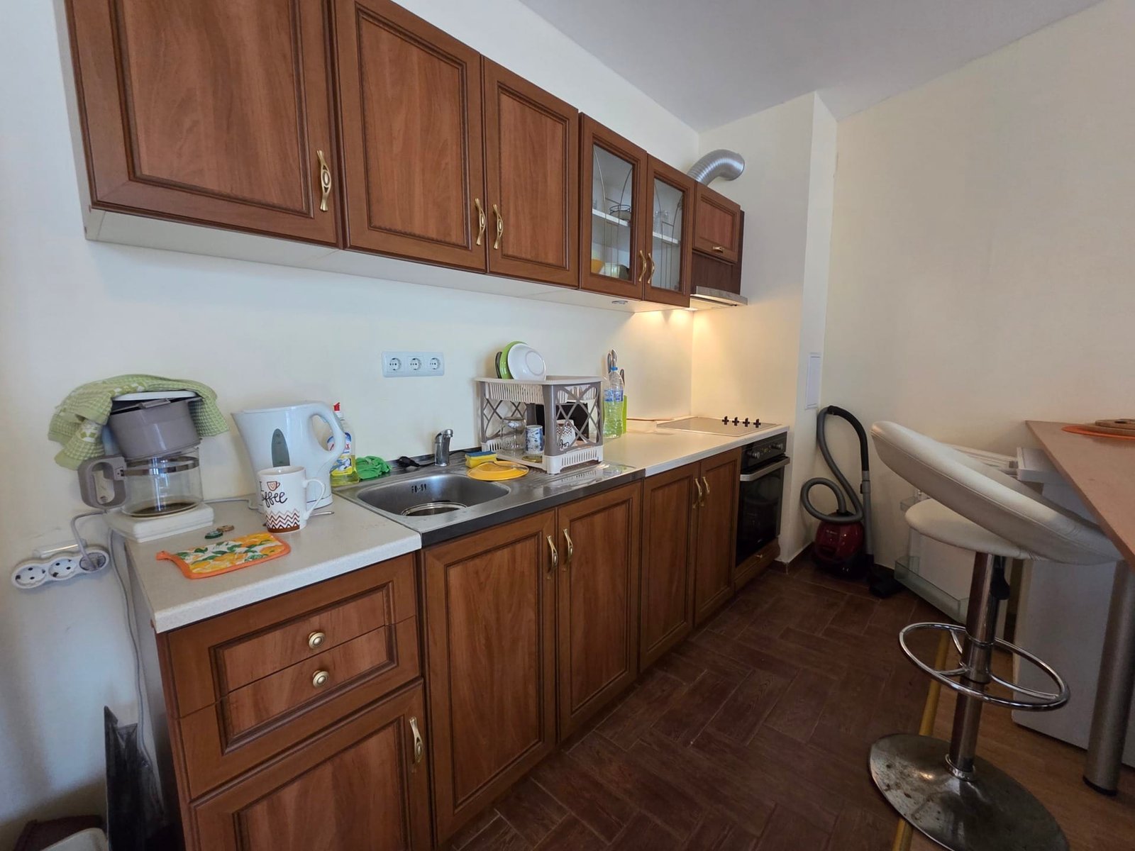 Кухня двухкомнатного апартамента в “Riviera Fort Beach” Современная кухня с деревянными шкафчиками, раковиной, плитой и барной стойкой в апартаменте Riviera Fort Beach.