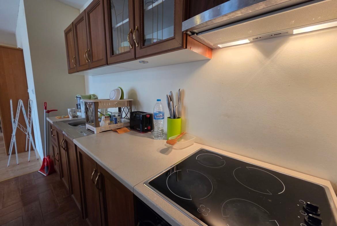 Современная кухонная зона с деревянными шкафчиками, варочной панелью, раковиной и бытовой техникой, подготовленная для отдыха.