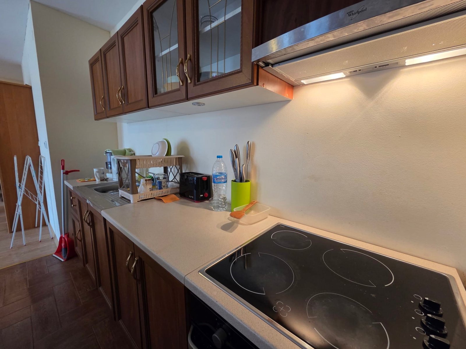 Кухня двухкомнатного апартамента Riviera Fort Beach Современная кухонная зона с деревянными шкафчиками, варочной панелью, раковиной и бытовой техникой, подготовленная для отдыха.