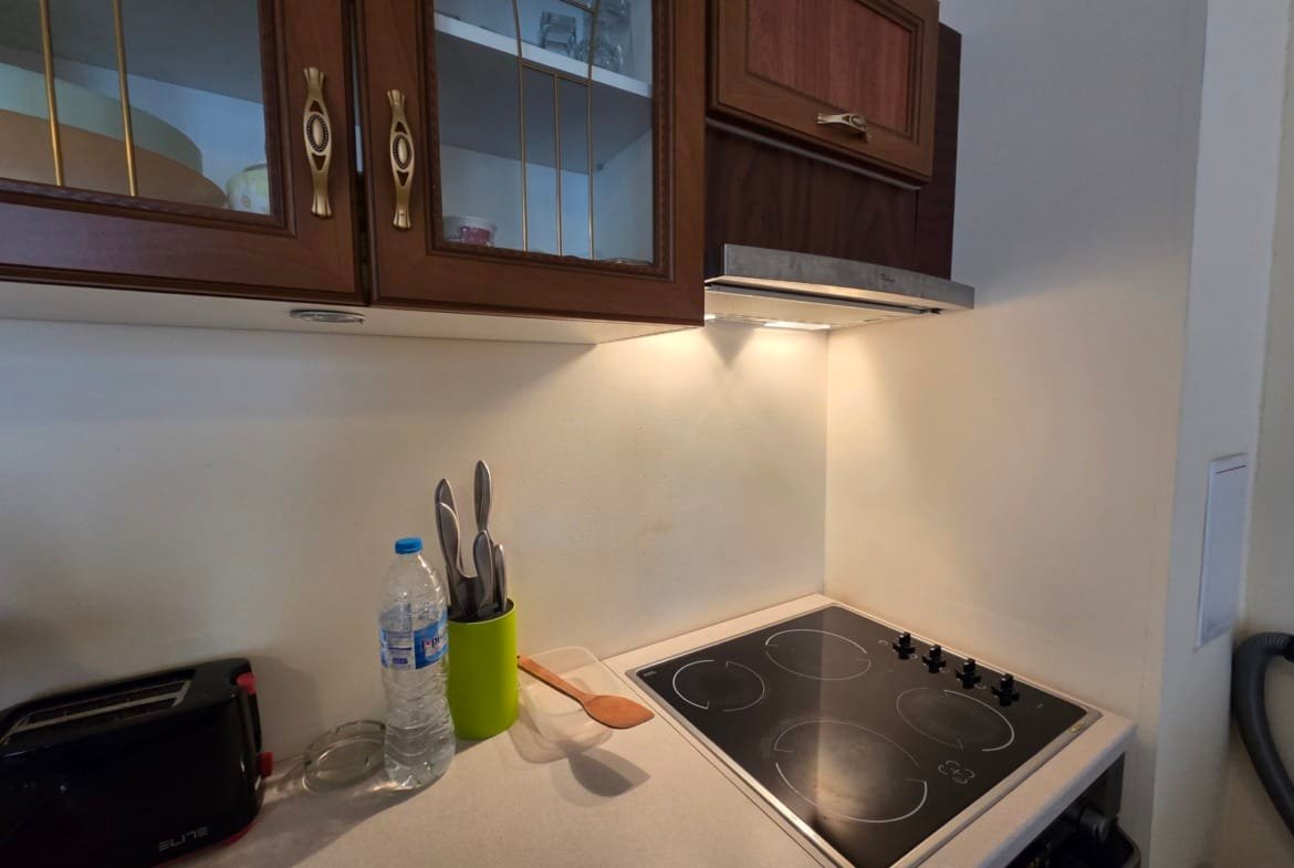 Современная кухня в апартаменте с плитой, столовыми приборами и бутылкой воды, светлым интерьером и удобным пространством.