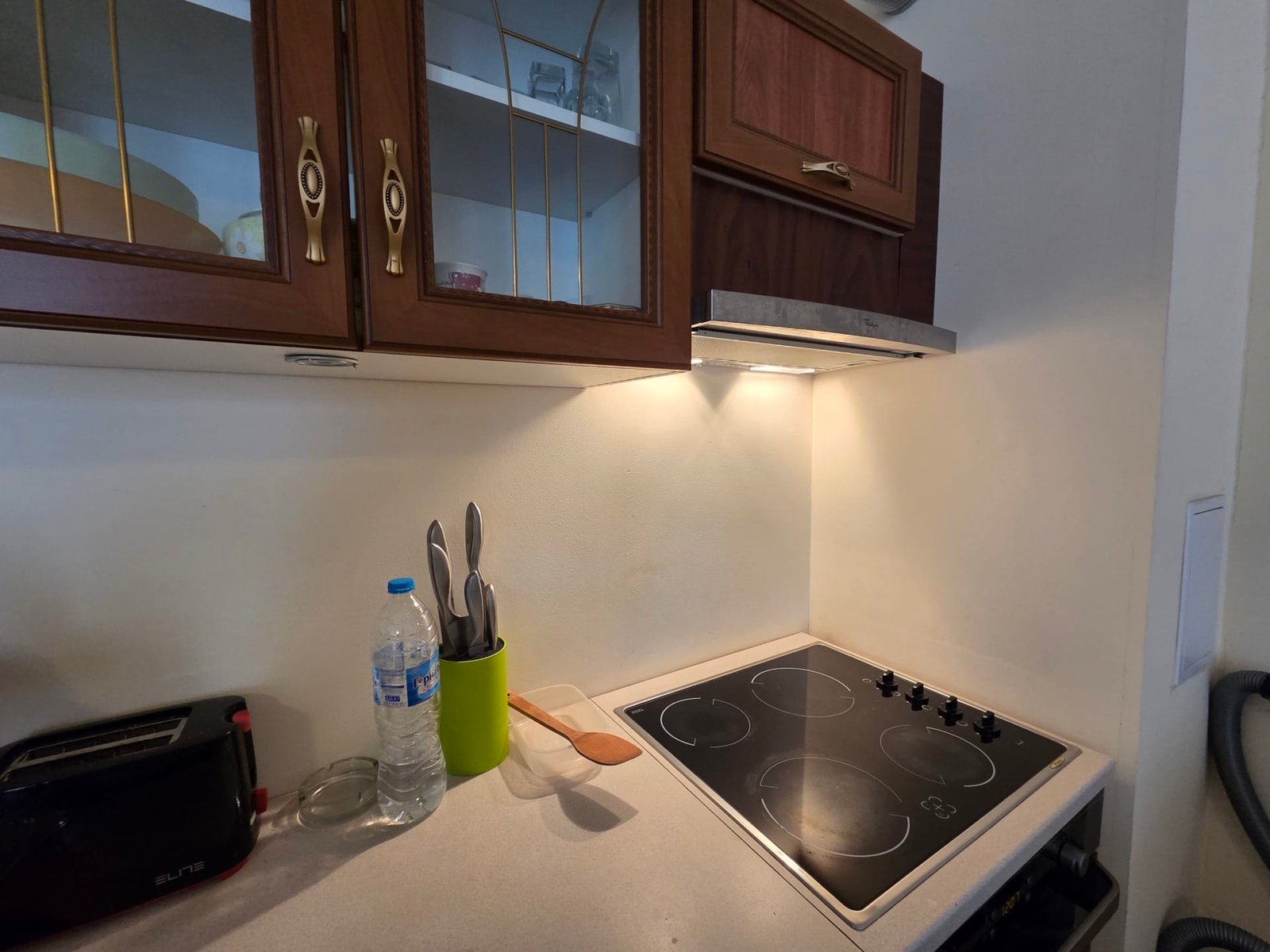 Кухня двухкомнатного апартамента в Riviera Fort Beach Современная кухня в апартаменте с плитой, столовыми приборами и бутылкой воды, светлым интерьером и удобным пространством.