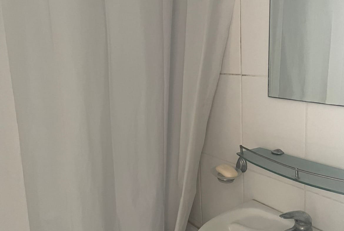 Санузел с душевой занавеской, раковиной и зеркалом, светлые плитки, современный стиль.