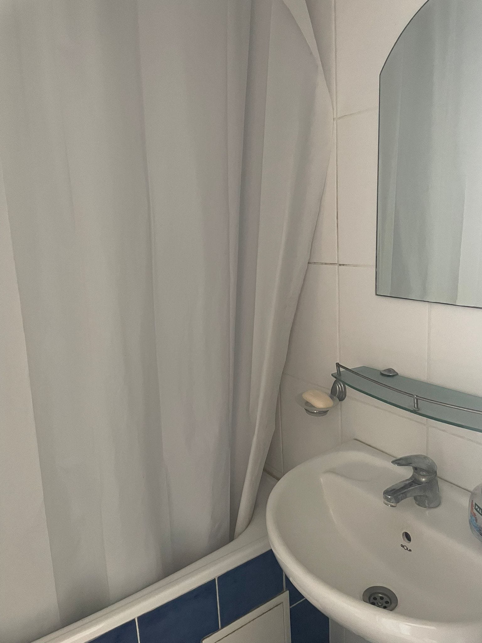 Санузел с душевой занавеской, раковиной и зеркалом, светлые плитки, современный стиль.