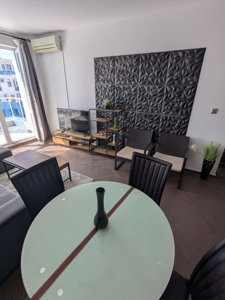 Современный интерьер двухкомнатного апартамента с стильной мебелью, стеклянным столом и телевизором на фоне текстурной стены.