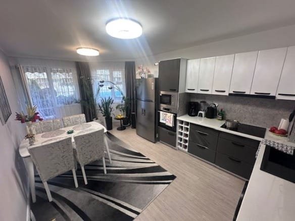 Современная кухня с обеденной зоной, оборудованная техникой, столом и стульями, оформленная в светлых тонах.