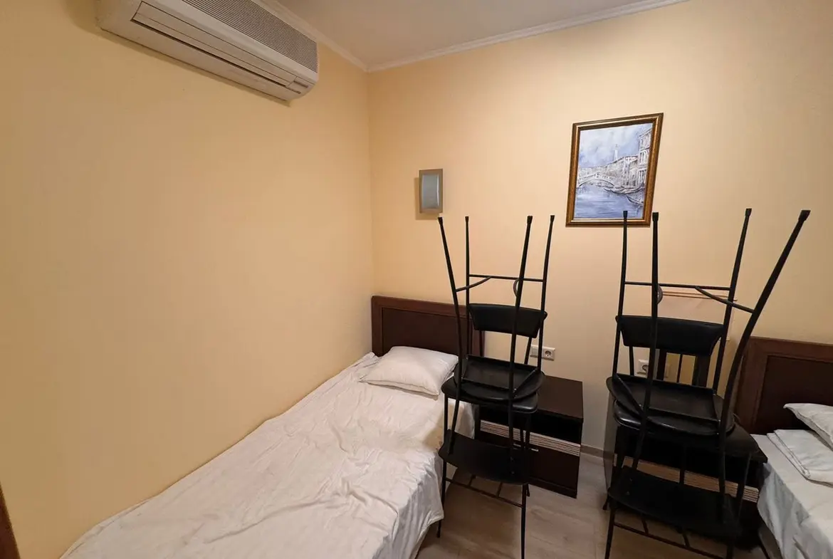 Трехкомнатный апартамент в Sunset Resort – комната с кроватью и стульями Трехкомнатный апартамент с одним спальным местом и стульями, сложенными на кровати, жёлтыми стенами и кондиционером.