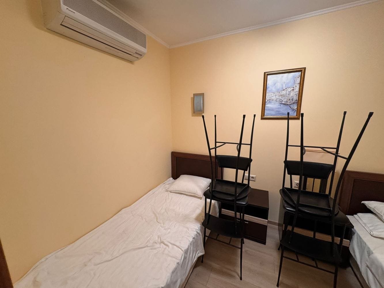 Трехкомнатный апартамент в Sunset Resort – комната с кроватью и стульями Трехкомнатный апартамент с одним спальным местом и стульями, сложенными на кровати, жёлтыми стенами и кондиционером.