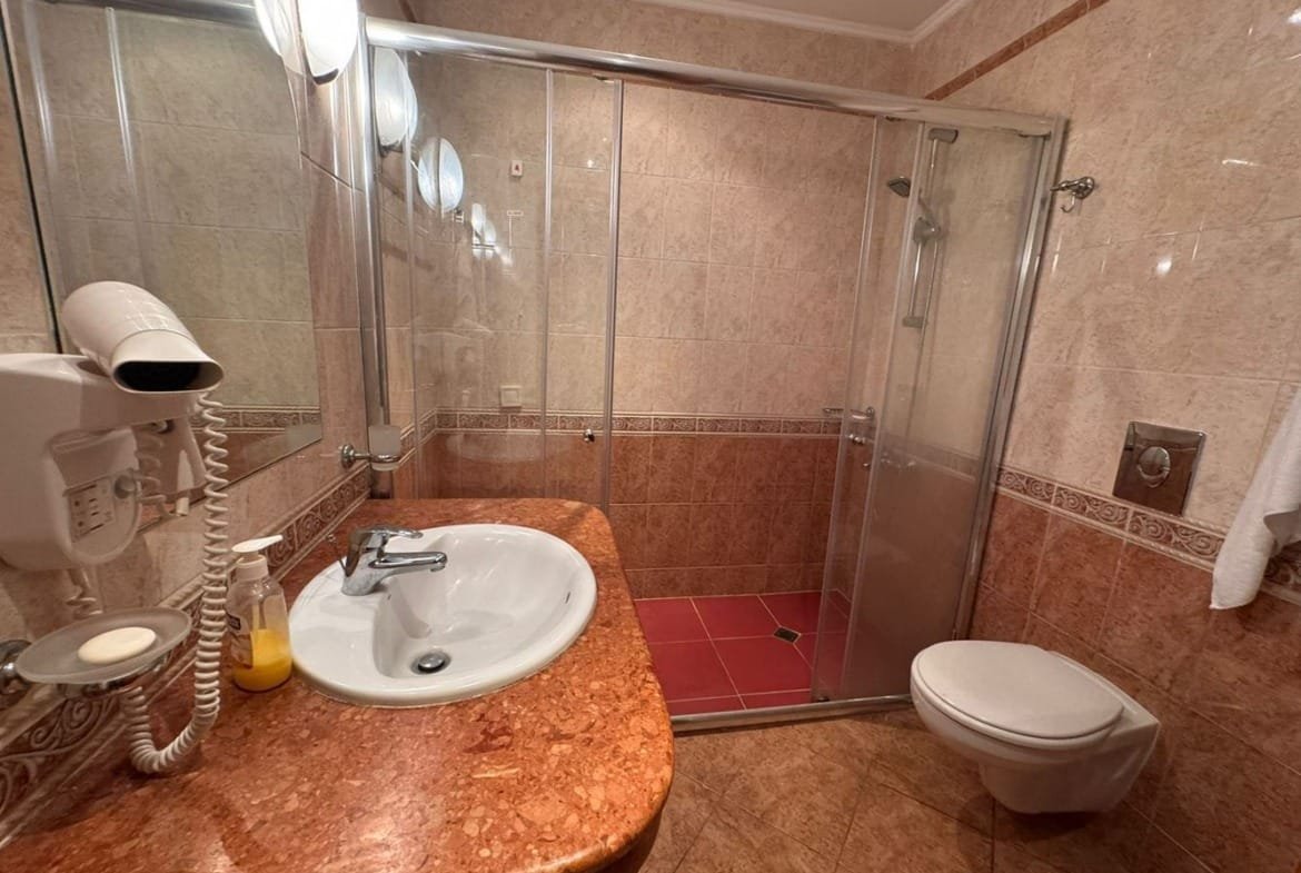 Современный санузел с душевой кабиной, умывальником с мраморной столешницей и сантехникой в бежевых тонах.