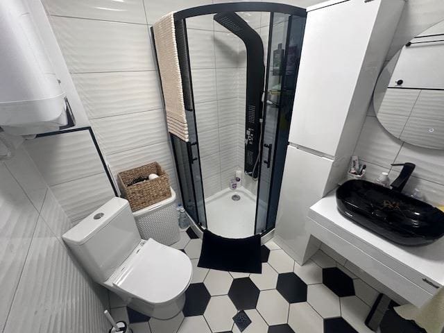 Современная ванная комната с душевой кабиной, унитазом и стильной раковиной на черно-белом плиточном полу.