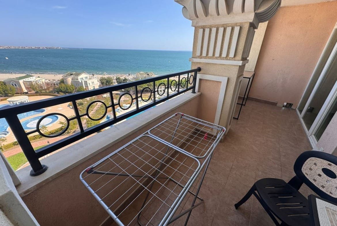 Балкон с сушилкой и стульями, вид на море и бассейн комплекса Sunset Resort, солнечное небо и чистая вода.