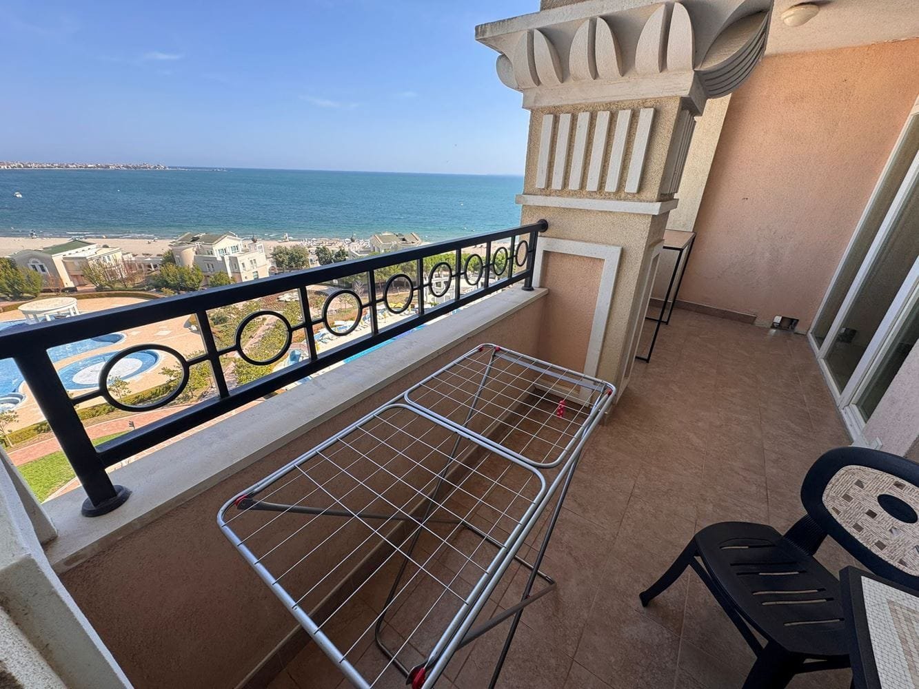 Балкон с видом на море в апартаменте “Sunset Resort” Балкон с сушилкой и стульями, вид на море и бассейн комплекса Sunset Resort, солнечное небо и чистая вода.