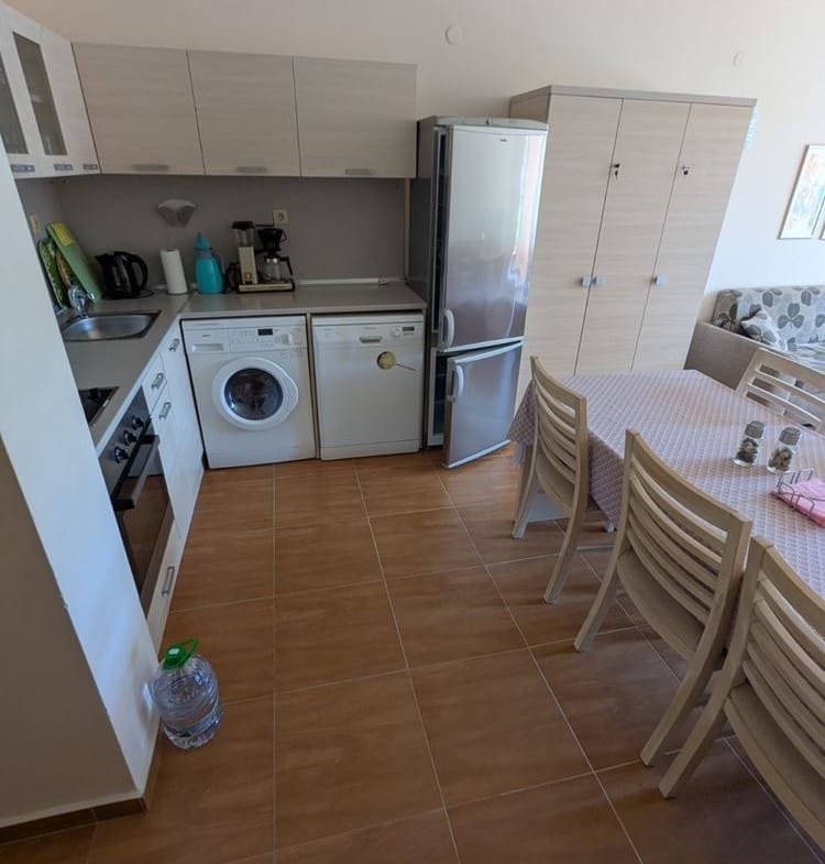 Кухня с современными встроенными шкафами, стиральной машиной, холодильником и обеденным столом в трехкомнатном апартаменте.