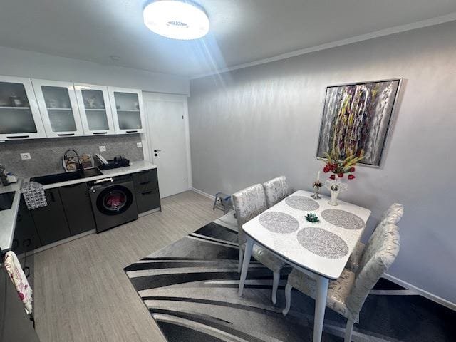 Современная кухня с обеденным столом и стульями, стиральной машиной и стильным декором на стенах. Теплые оттенки и уютная атмосфера.