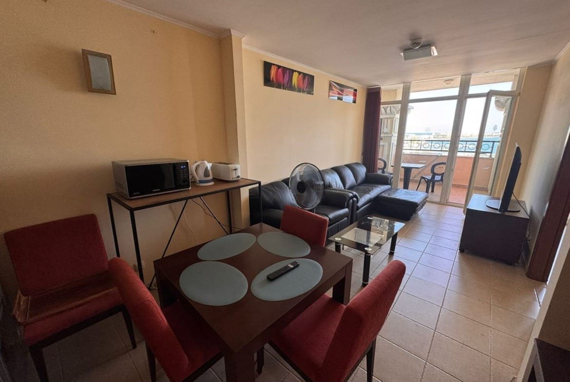 Трехкомнатный апартамент с диваном, обеденным столом и кухонной зоной, выход на балкон с видом на море.