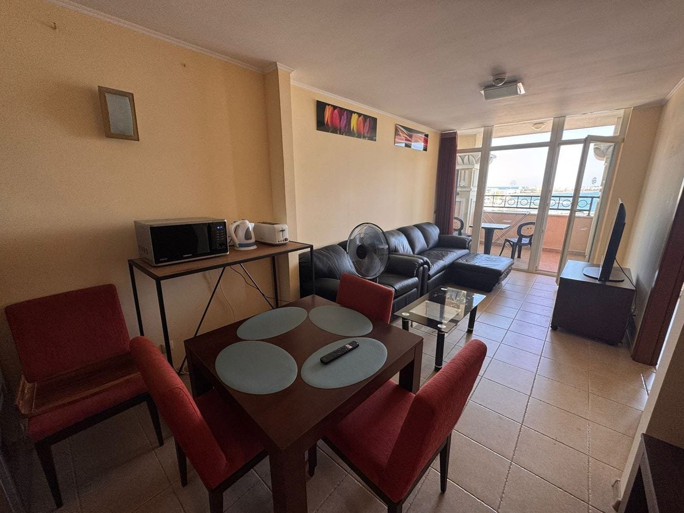 Трехкомнатный апартамент в “Sunset Resort” — уютная гостиная с кухней Трехкомнатный апартамент с диваном, обеденным столом и кухонной зоной, выход на балкон с видом на море.