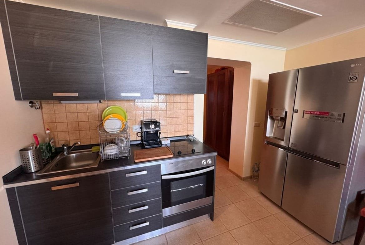 Современная кухня в трехкомнатном апартаменте: черные шкафы, плита, холодильник, совмещенный с обеденной зоной, плитка.