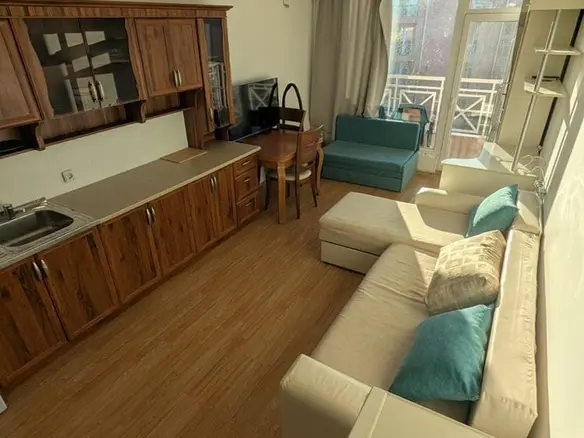 Светлая студия с кухонным уголком, обеденным столом, диваном, креслом и балконной дверью. Деревянная отделка и уютные цвета.