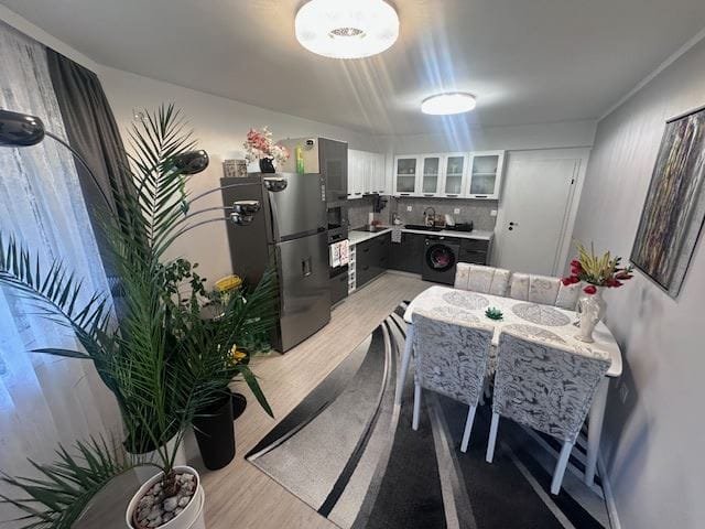 Современная кухня-студия с обеденной зоной, холодильником и стиральной машиной, оформлена в светлых тонах.