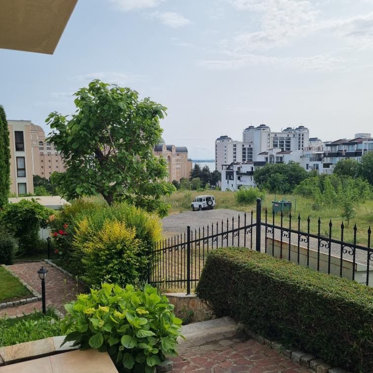 Вид на территорию комплекса Relax Holiday с зелеными насаждениями, домами и машиной на парковке вдали.