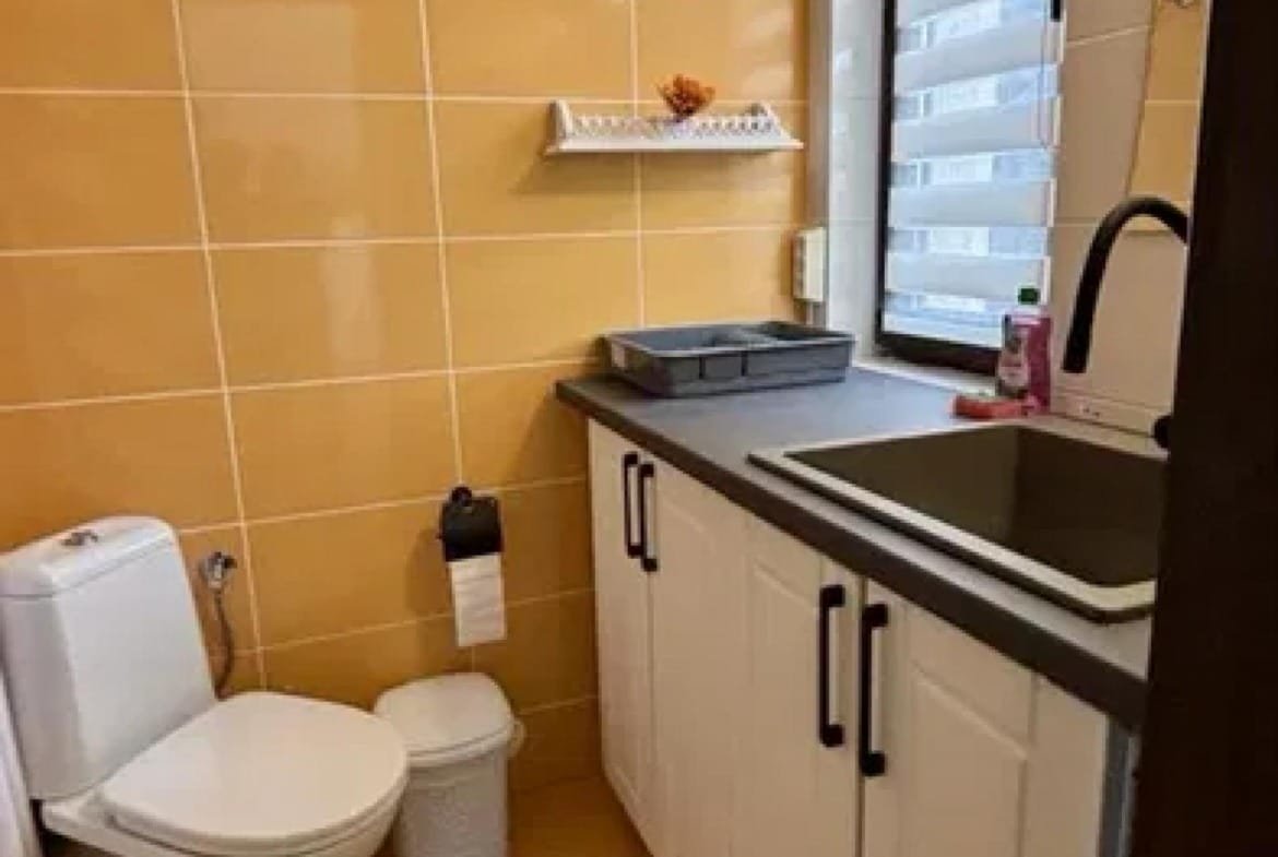 Современная ванная комната с туалетом, раковиной и плиткой жёлтого цвета. Просторное помещение с минималистичным дизайном.