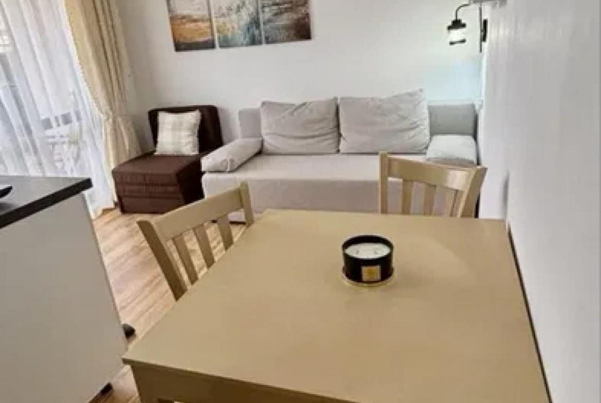 Современная студия с диваном, столом и стульями, оформленная в светлых тонах, с большим окном и современными аксессуарами.