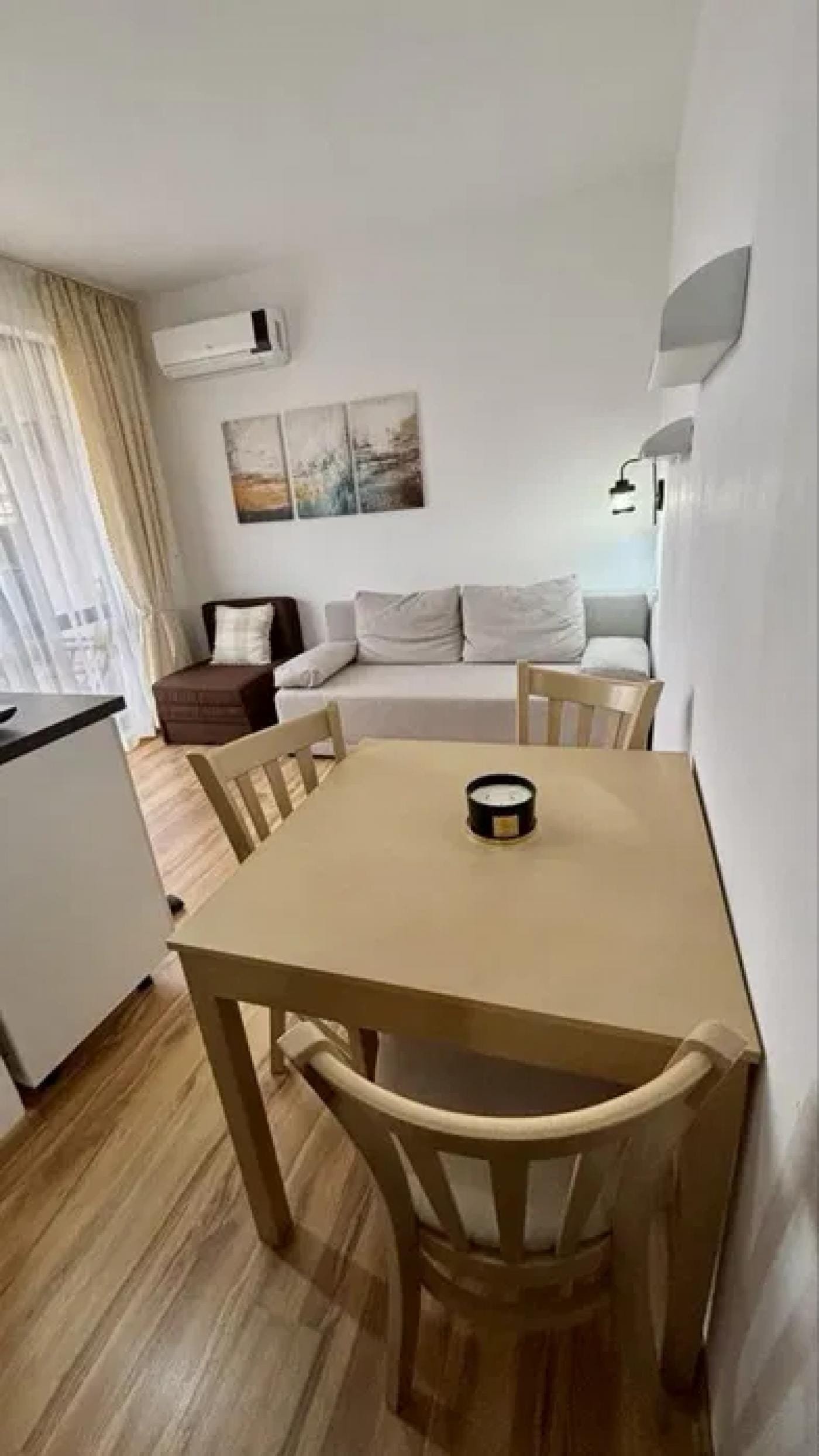 Современная студия с диваном, столом и стульями, оформленная в светлых тонах, с большим окном и современными аксессуарами.