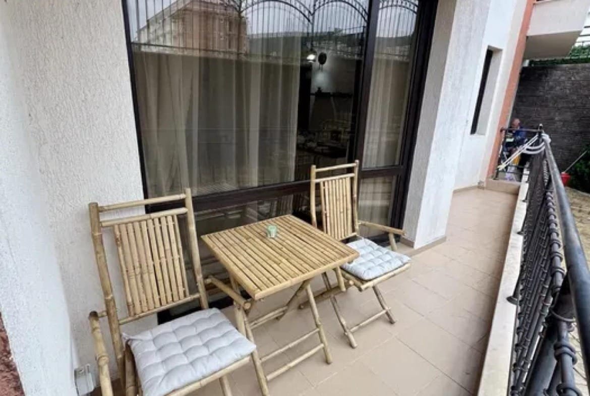 Балдахин с двумя стульями и столом на балконе, рядом с окнами, оформлен в светлых тонах.