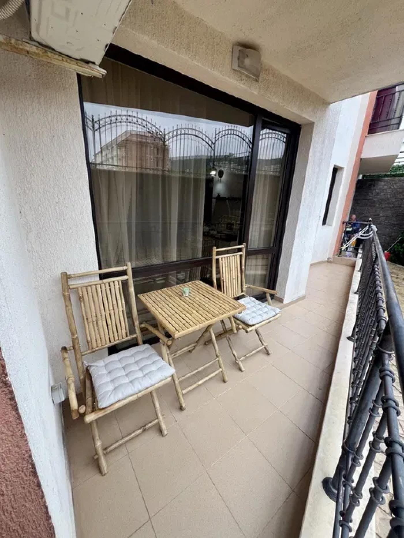 Балдахин с двумя стульями и столом на балконе, рядом с окнами, оформлен в светлых тонах.