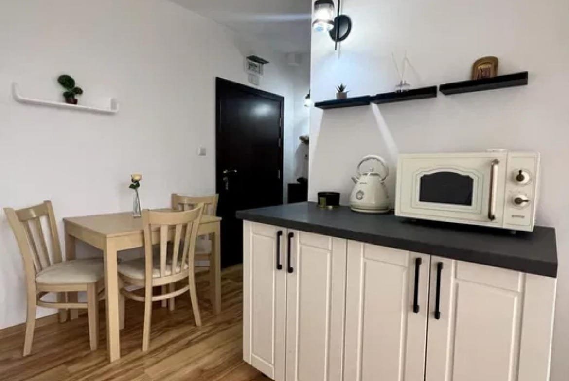 Кухня студии с деревянным столом, стульями, микроволновкой и черной столешницей на фоне светлых стен и пола.