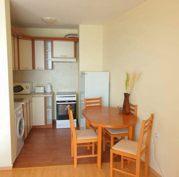 Трехкомнатный апартамент с кухней и обеденной зоной, деревянный стол и стулья, светлые тона, современная бытовая техника.