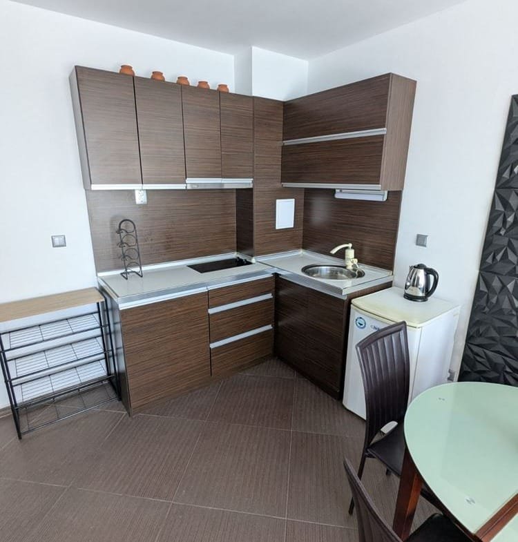 Современная кухня в двухкомнатном апартаменте с темными шкафчиками, плитой, раковиной и столом для приема пищи.