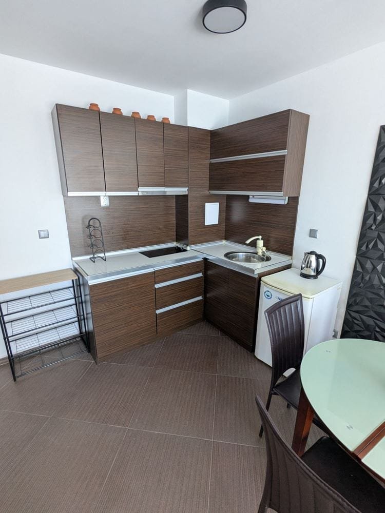 Современная кухня в двухкомнатном апартаменте с темными шкафчиками, плитой, раковиной и столом для приема пищи.