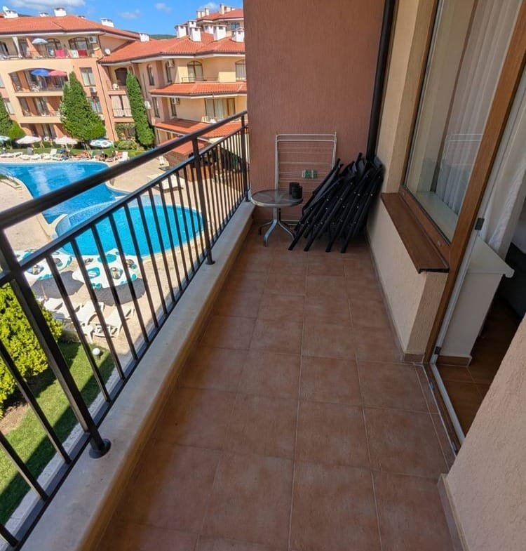 Балкон с видом на бассейн, с мебелью и стульями, окружённый зеленью и апартаментами комплекса Panorama Dreams.