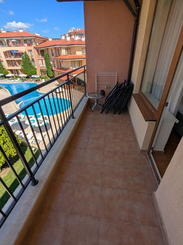 Балкон с видом на бассейн, с мебелью и стульями, окружённый зеленью и апартаментами комплекса Panorama Dreams.