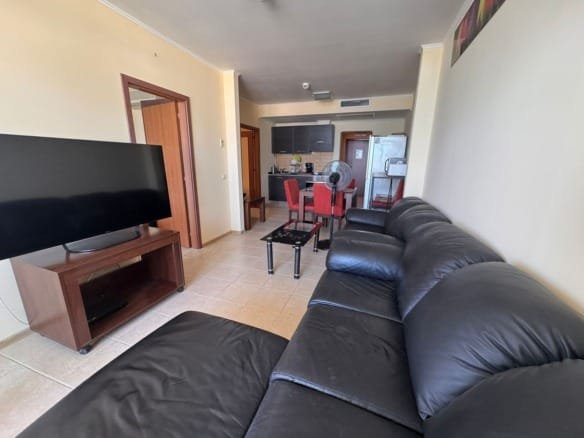 Современный интерьер трехкомнатного апартамента с черным диваном, телевизором и кухонной зоной в комплексе Sunset Resort.