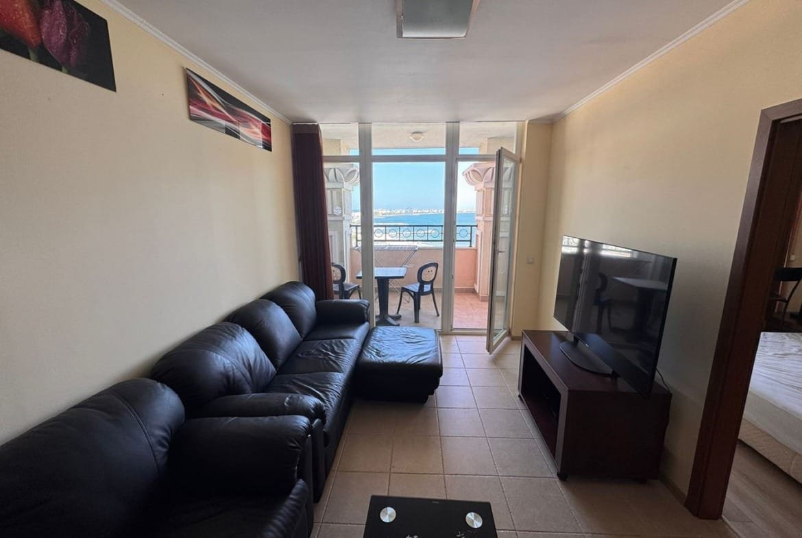 Современная гостиная с черным диваном, телевизором и выходом на балкон с видом на море, яркими стенами и стильной мебелью.