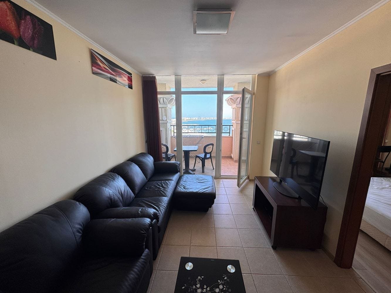 Трехкомнатный апартамент в “Sunset Resort” с видом на море Современная гостиная с черным диваном, телевизором и выходом на балкон с видом на море, яркими стенами и стильной мебелью.